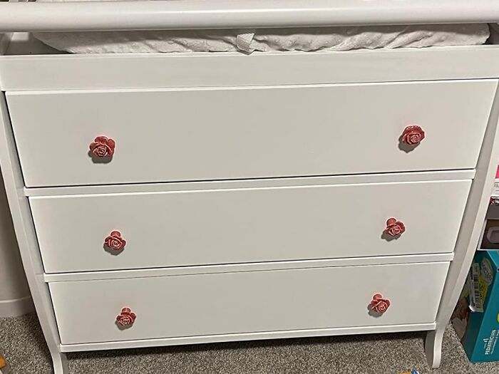 White dresser with pink rose-shaped drawer handles in a cozy room, adding a seriously sweet and charming touch.