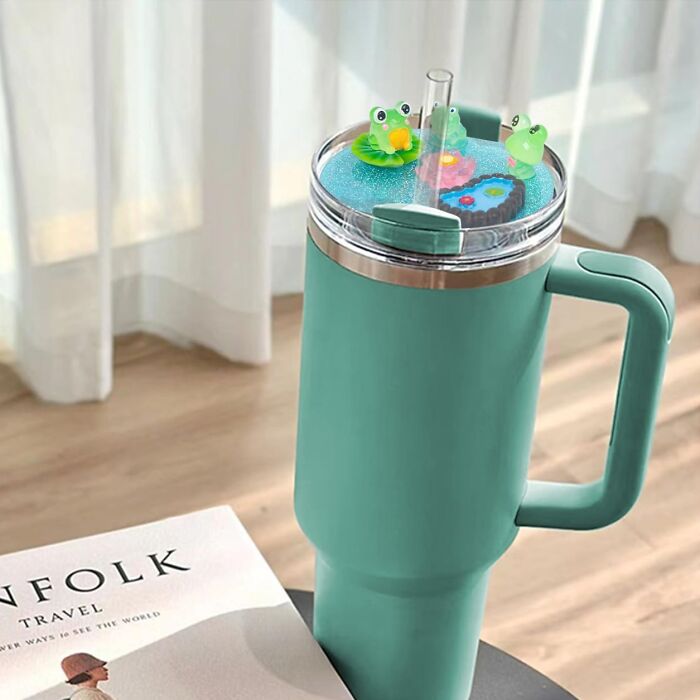 Teal travel mug with cute frog decorations on the lid, adding a seriously sweet and charming touch to your drinkware.