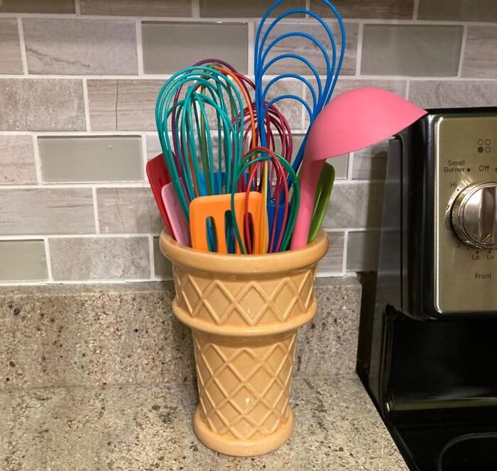 Kitchen utensils in colorful silicone stored in a unique ice cream cone-shaped holder, adding a sweet touch to the space.