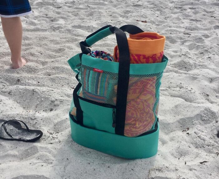 Beach bag with towels and essentials on sand, perfect for conquering sun, sand, and snack attacks on your beach day.