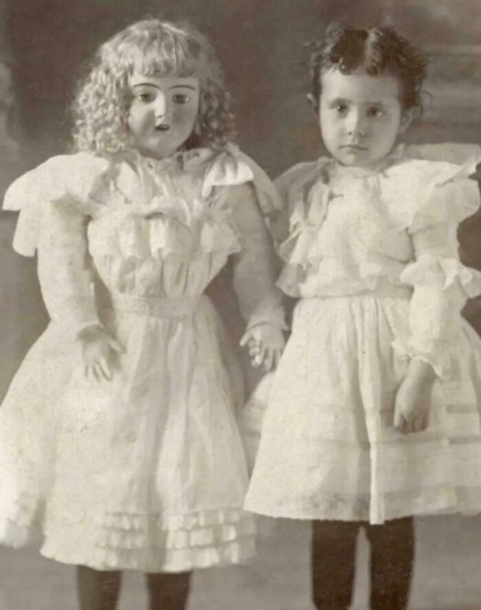 Victorian times strange moment showing a girl holding hands with a life-sized doll dressed in matching old-fashioned clothing.