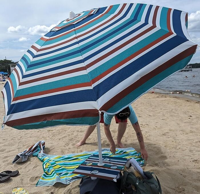 Striped beach umbrella and towel set up on sandy shore for sun, sand, and snack attacks on a beach day.