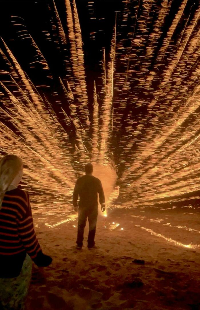 Person silhouetted against bright sparks exploding outward in one of the most unreal photographs at night.