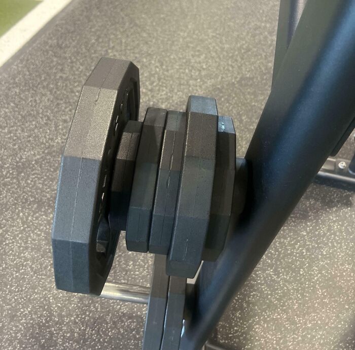 Stacked gym weight plates loosely arranged on a barbell, illustrating an annoying gym moment with equipment.
