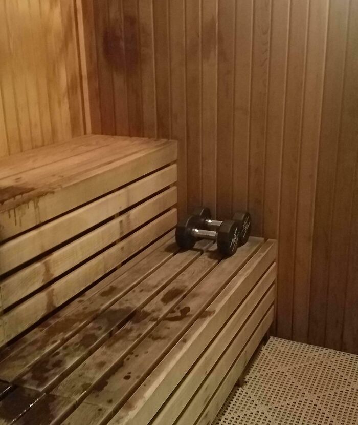 Wooden gym sauna benches with water stains and a pair of dumbbells, highlighting annoying gym moments.