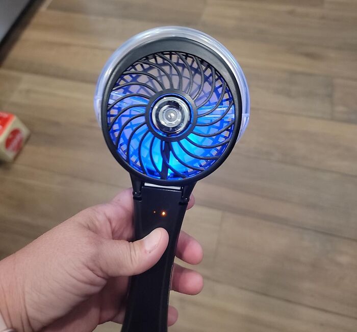 Hand holding a portable handheld fan with blue LED light, a perfect beach day find to conquer sun and sand.
