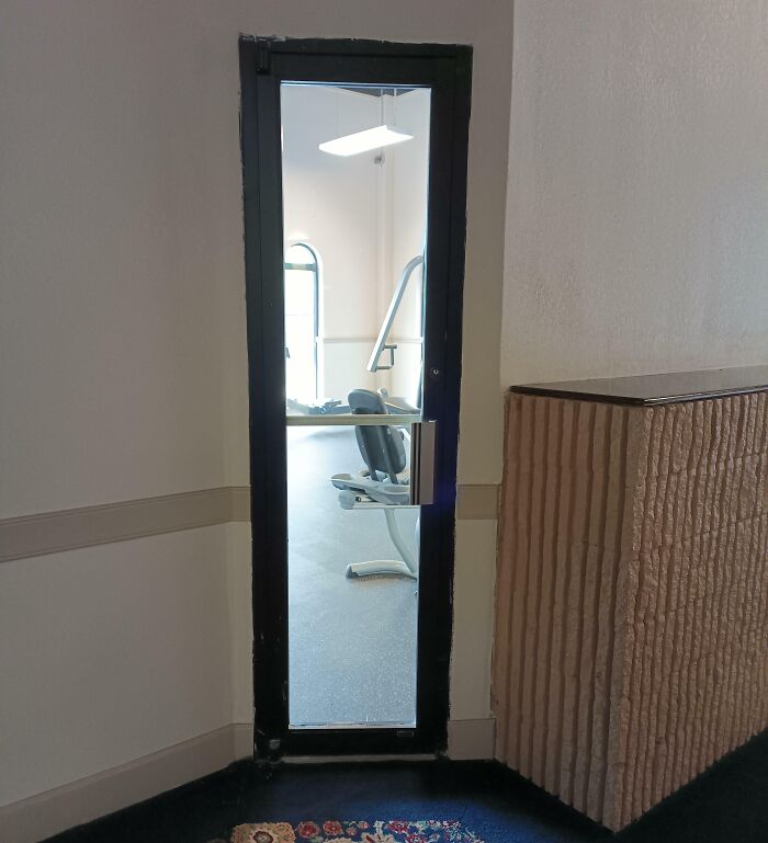 Narrow gym door with a mirror reflecting exercise equipment, illustrating annoying gym moments and workout challenges.