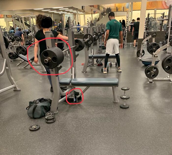Gym scene showing heavy weights left on bench press and a phone placed on the floor causing annoying gym moments.