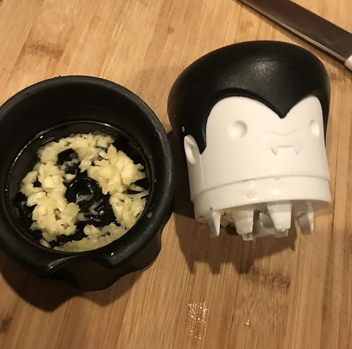 Garlic press with minced garlic inside on wooden cutting board, essential adulting starter pack for first apartment cooking.