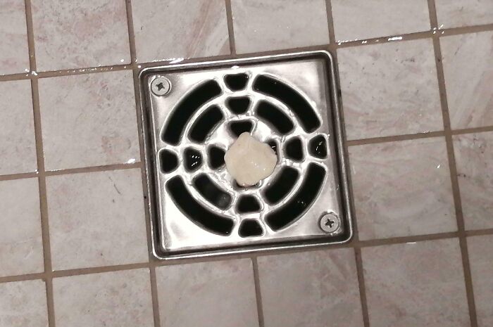 Chewing gum stuck in a gym shower drain on tiled floor representing annoying gym moments.