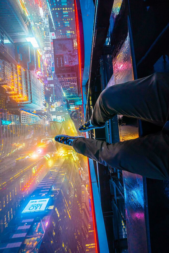 Feet dangling off a rooftop at night above a glowing cityscape showcasing unreal photographs of urban heights.