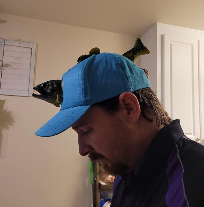 Man wearing a blue cap with bizarre fish decorations indoors, illustrating bizarre finds affecting your bank account.