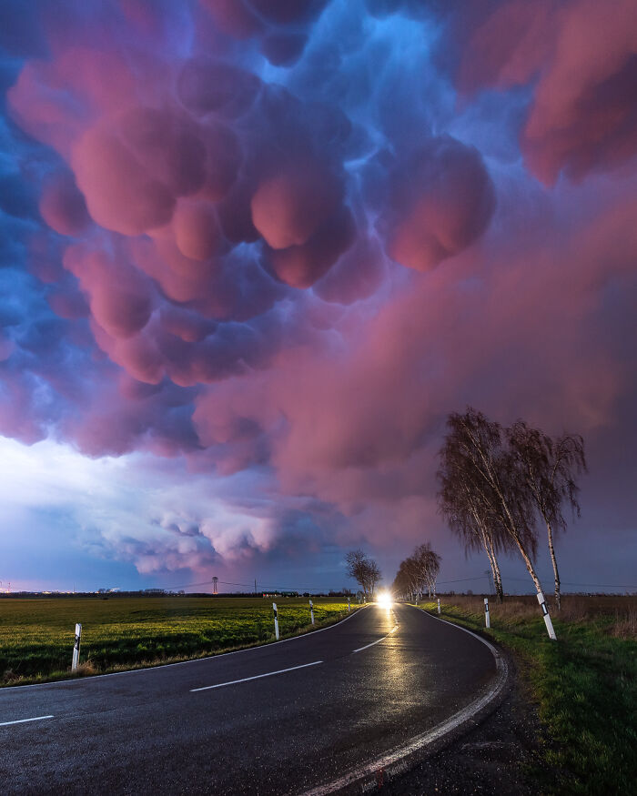 Unreal photographs showing a dramatic sky with mammatus clouds over a curved road and illuminated countryside at dusk.