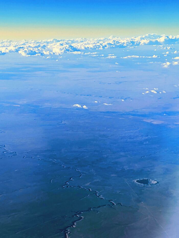 Aerial view of a vast landscape with a large crater and scattered clouds, showcasing unreal photographs.