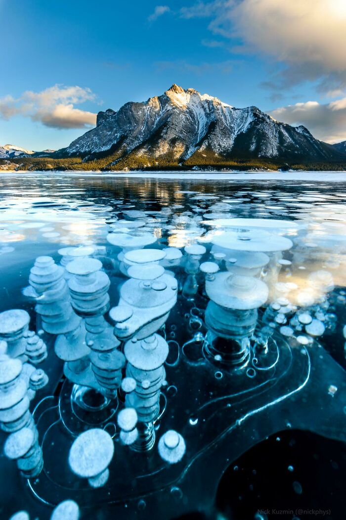 Unreal photographs showing frozen methane bubbles beneath clear ice with a mountain landscape in the background.