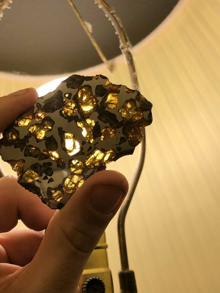 Hand holding a translucent rock with golden fragments illuminated by a lamp, showcasing unreal photographs quality.