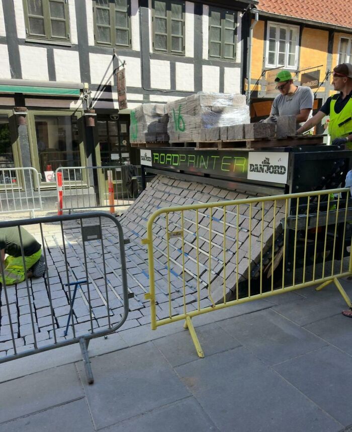 Machine printing cobblestones in an urban setting with workers installing them, showcasing unreal photographs of street construction.