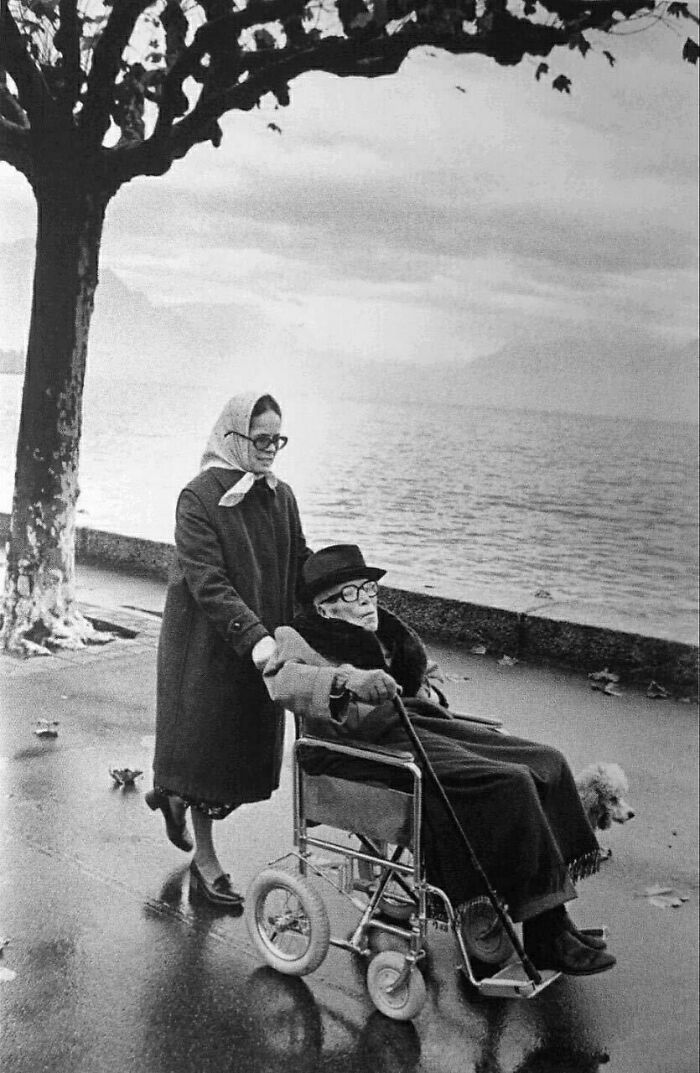 Elderly man in wheelchair with woman assisting by a lakeside, one of the last known photos of famous people.