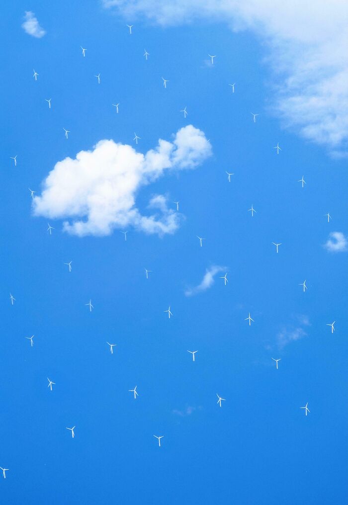 Unreal photograph of numerous tiny wind turbines scattered across a bright blue sky with white clouds.