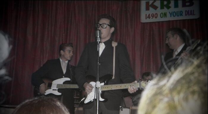 Musician performing with electric guitar and microphone on stage, one of the last known photos of famous people.