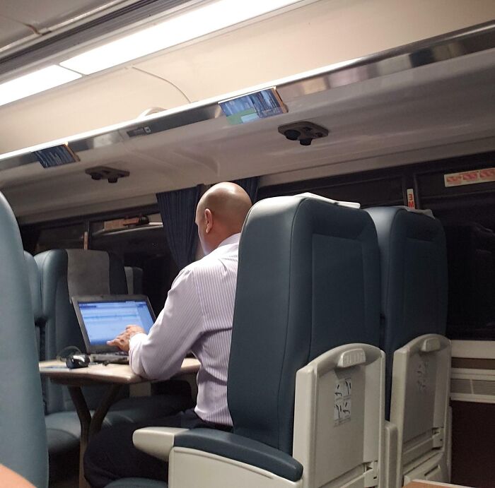 Man working on a laptop while sitting in a train seat, illustrating typical public transport passengers behavior.