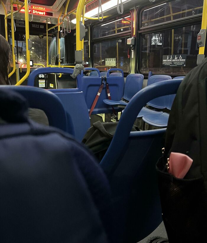 Interior view of a city bus at night with empty blue public transport seats and passengers standing nearby.