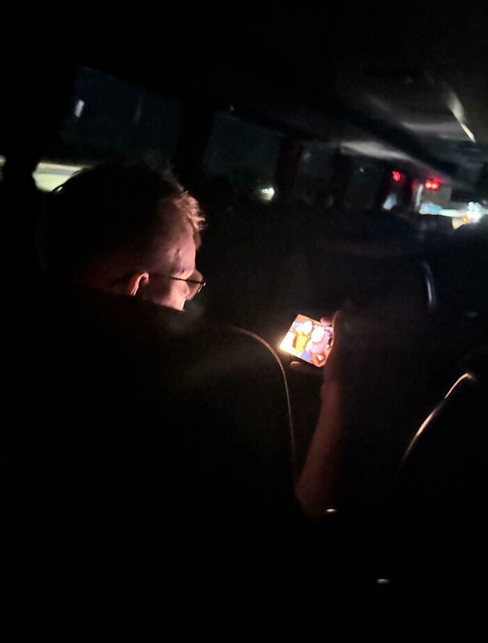 Passenger in dark bus cabin brightly illuminating others by watching video on phone screen, annoying public transport behavior.