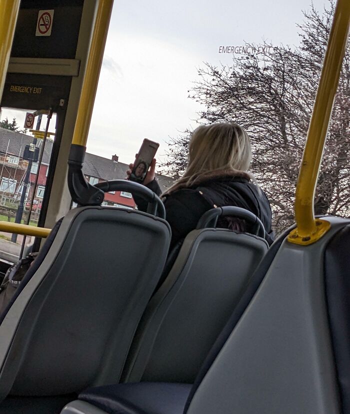 Passenger on public transport taking a selfie while seated near emergency exit signs during daytime ride.