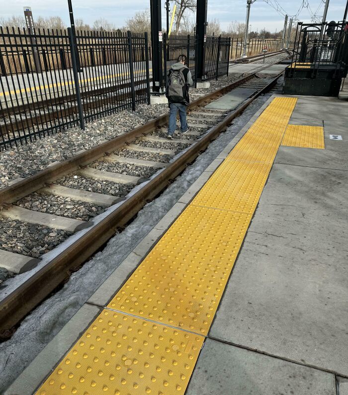 Passenger walking dangerously on train tracks at a public transport station displaying bad commuter behavior and safety risk.