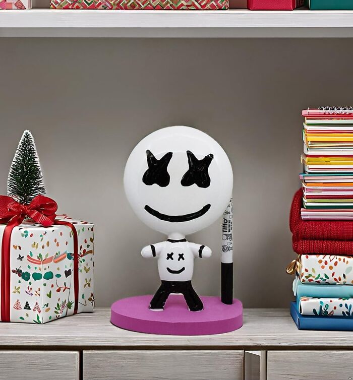 Unique office supplies figurine with marker holder, placed on a shelf next to colorful notebooks and a wrapped gift box.