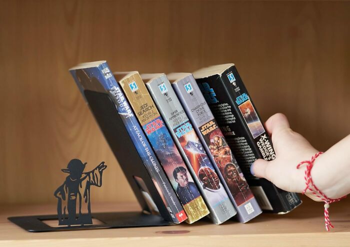 Hand reaching for Star Wars books held by Yoda-shaped office supplies bookends on a wooden shelf.