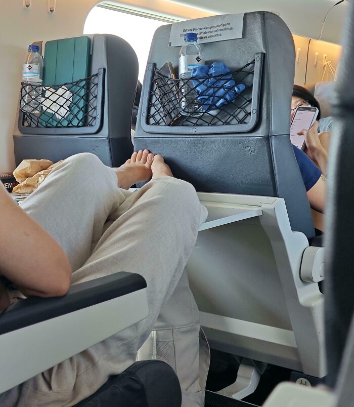 Passenger putting bare feet on public transport seat backrest, showing rude behavior of infuriating public transport passengers.