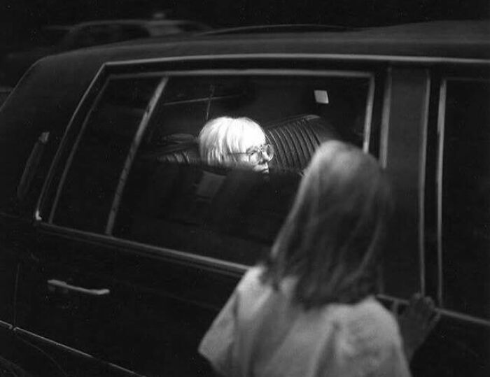 Black and white photo showing a famous person inside a car seen through the window with a child outside, last known photos.