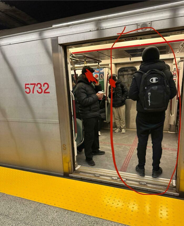Public transport passengers standing inside a subway train car wearing winter jackets and backpacks.