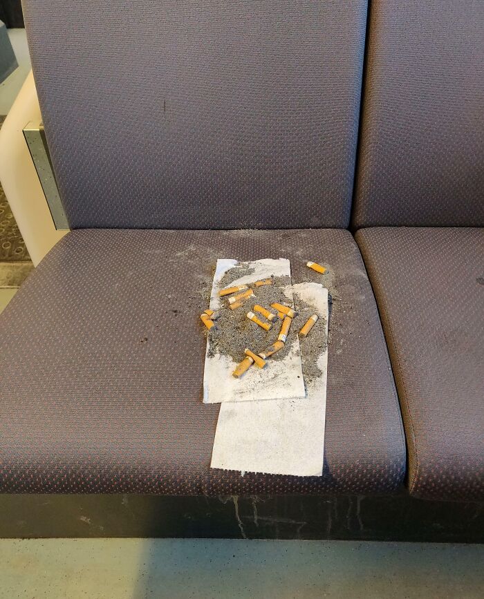 Public transport seat covered with cigarette butts and ashes left by careless passengers showing bad behavior.