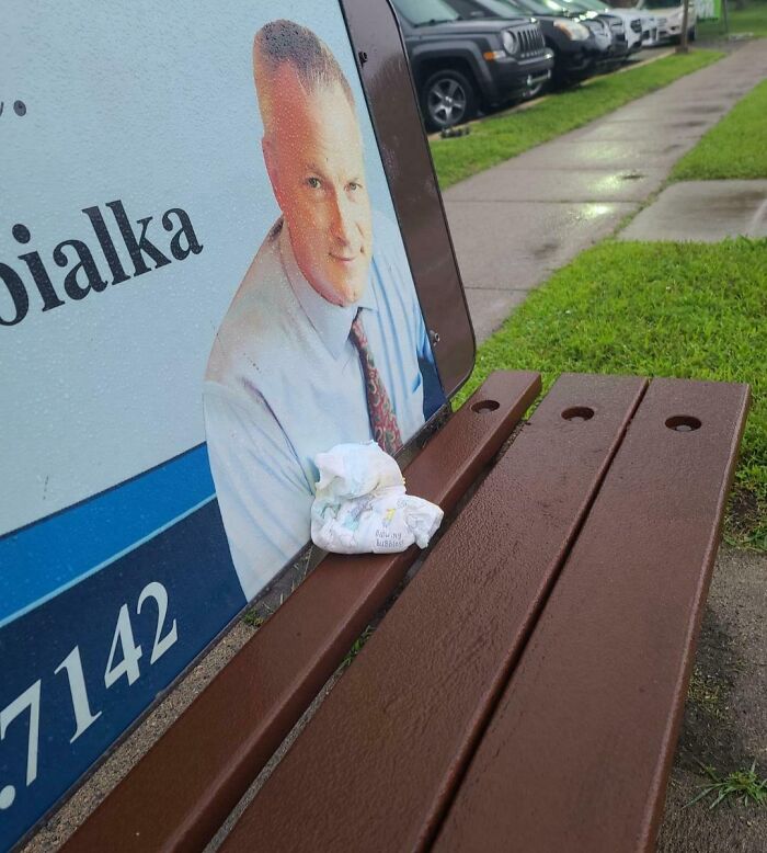 Crumpled diaper left on a wet public transport bench next to an advertisement, showing inconsiderate passenger behavior.