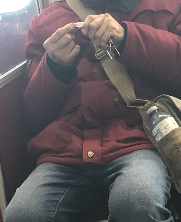 Passenger on public transport wearing a red jacket and jeans, holding a small object while sitting with a bag and water bottle.