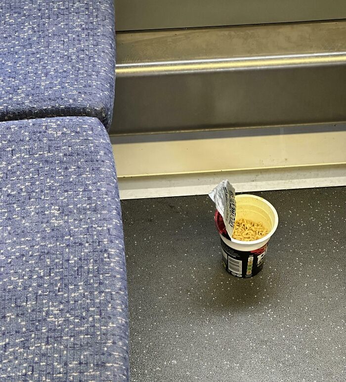 Cup of instant noodles left on the floor of a public transport vehicle, showing inconsiderate passenger behavior.