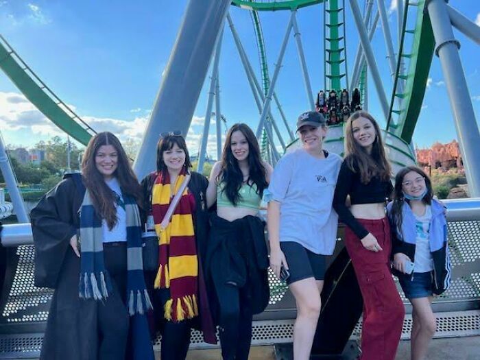Group of friends at amusement park with roller coaster in background, capturing a rare coincidence moment.