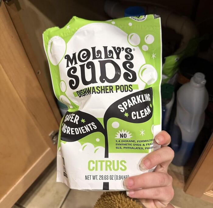 Hand holding Molly's Suds dishwasher pods in a kitchen with chemical-free and safer ingredients for clean dishes.
