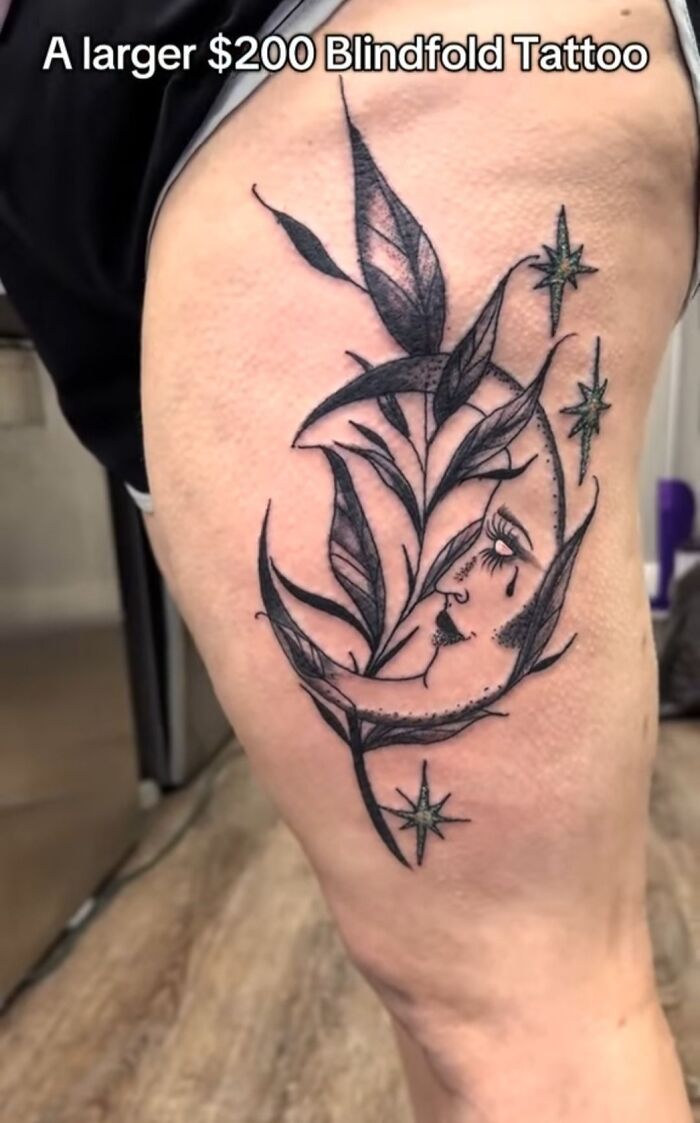 Black ink tattoo of a crescent moon with a face and leaves on a person's thigh showcasing hilariously bad tattoos.