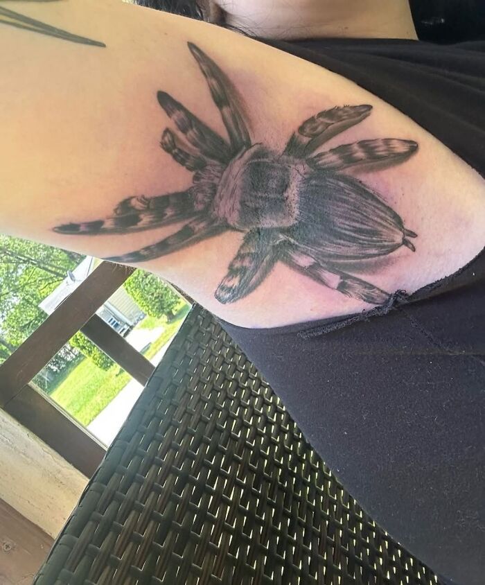 Tattoo of a large spider on upper arm showcasing a hilariously bad inkshaming example of body art.