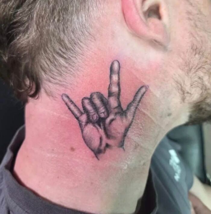 Close-up of a hilariously bad tattoo on a man’s neck showing a hand in a sign language gesture.