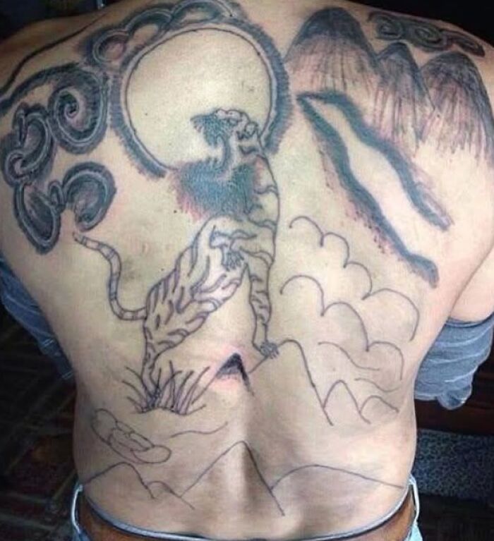 Back tattoo featuring a poorly drawn tiger, clouds, and abstract shapes, showcasing hilariously bad tattoos and inkshaming.