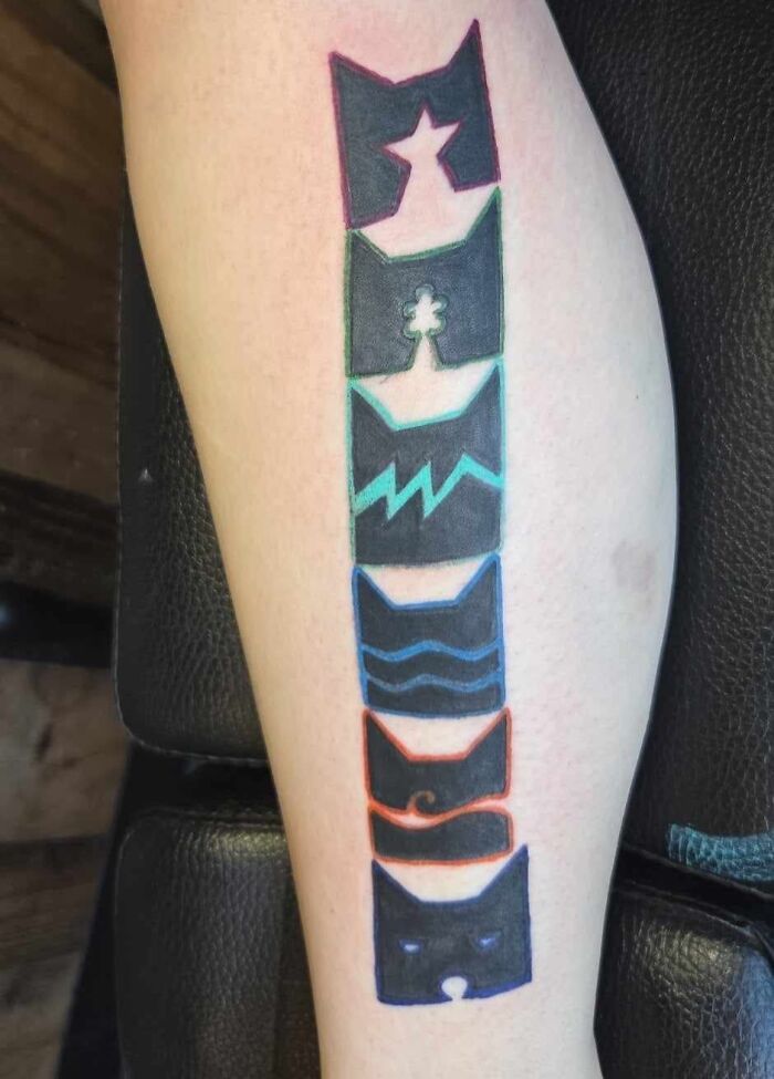 Abstract black ink tattoo on forearm with colorful outline featuring various shapes and symbols in a vertical design.
