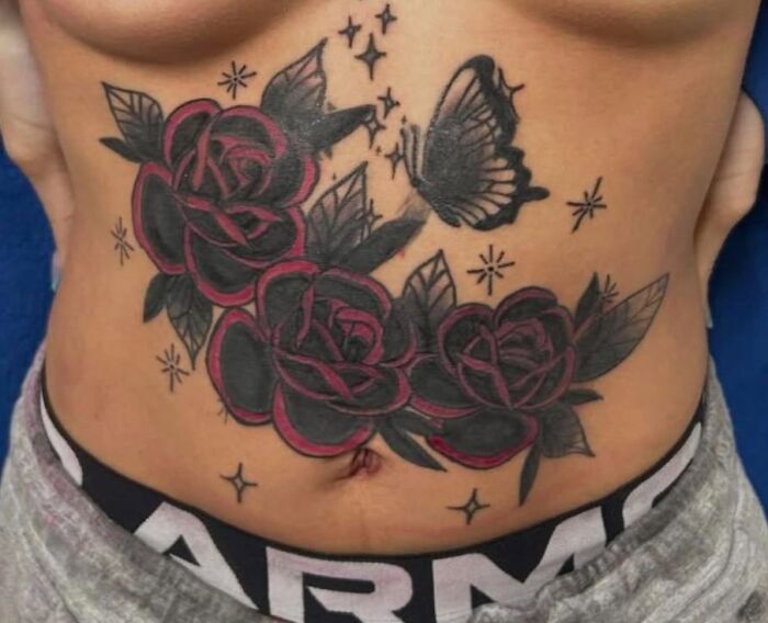 Tattoo of three dark roses and a butterfly on a person's lower abdomen with scattered star designs, example of bad tattoos.
