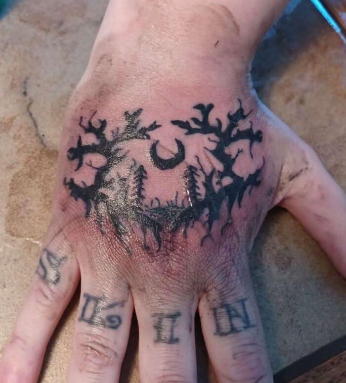 Hand tattoo with a poorly done forest and moon design, an example of hilariously bad tattoos and inkshaming fails.
