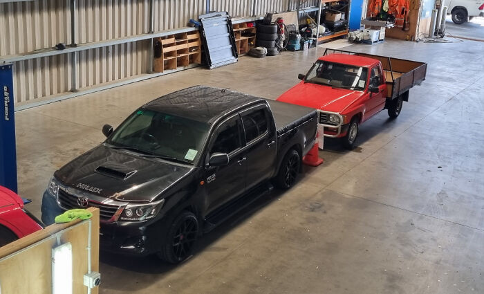 Black modern pickup truck parked next to a vintage red flatbed truck in a spacious garage comparison pics