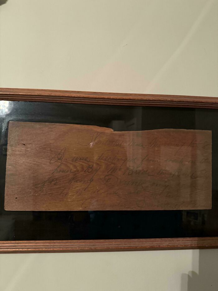 Faded historical memento on a wooden plaque with handwritten text, preserved and framed as a rare found artifact.