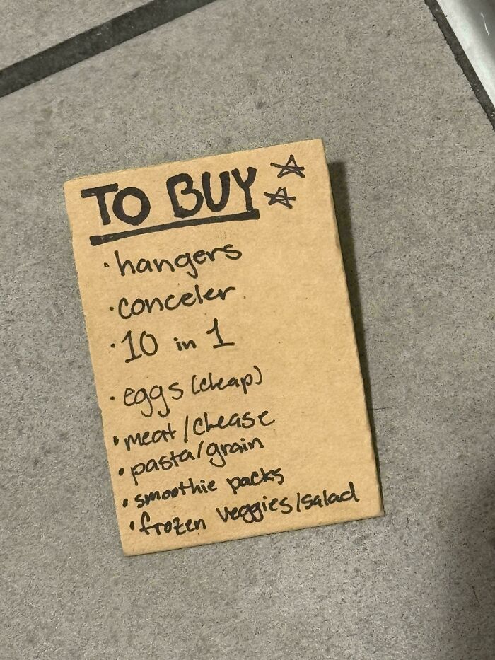 Handwritten to buy list on cardboard with items like hangers, concealer, eggs, and frozen veggies found as a historical memento.